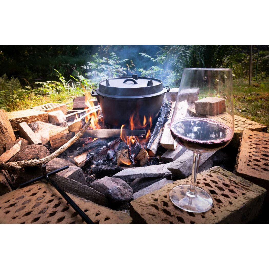 Ein Dutch Oven über einem Lagerfeuer und ein Glas Rotwein