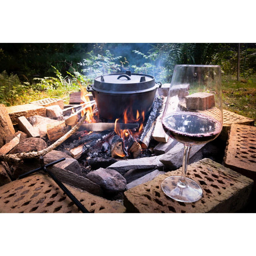 Ein Dutch Oven über einem Lagerfeuer und ein Glas Rotwein