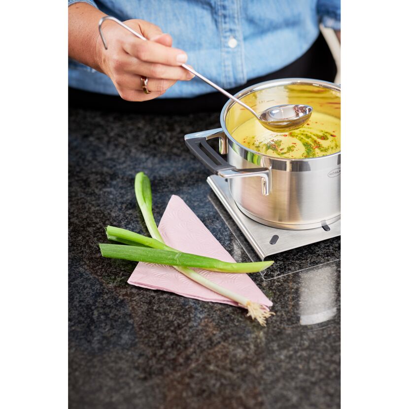 Person schöpft Suppe mit Schöpflöffel aus Topf.