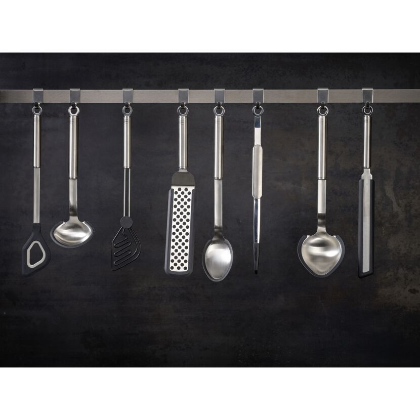 Sechs verschiedene Küchenhelfer hängen an einer schwarzen Wand.