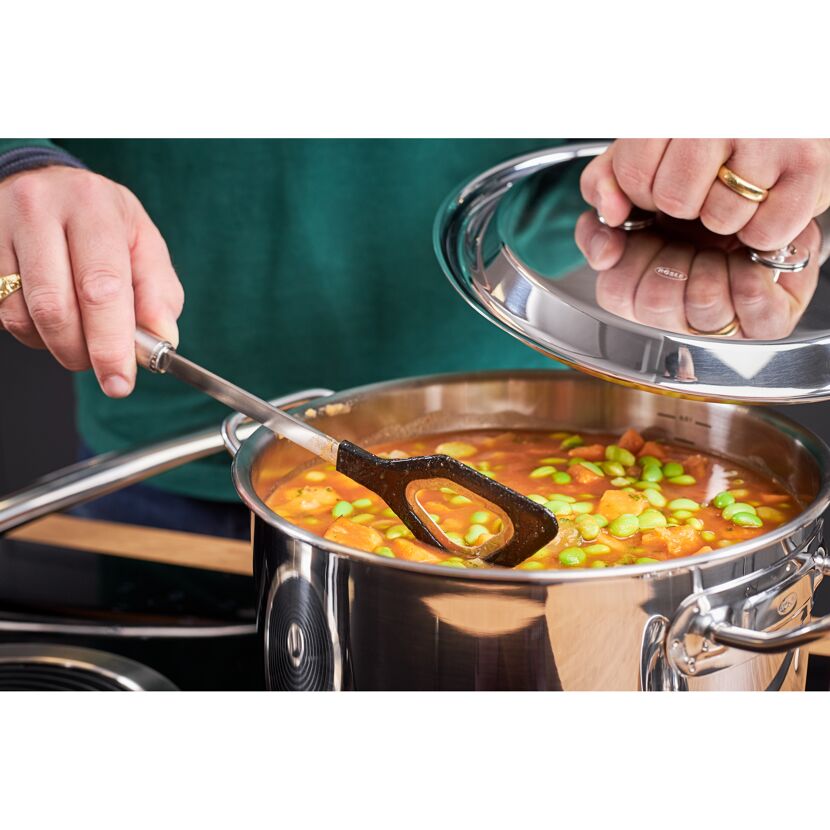 Person rührt mit einem Kochlöffel Suppe in einem Topf um