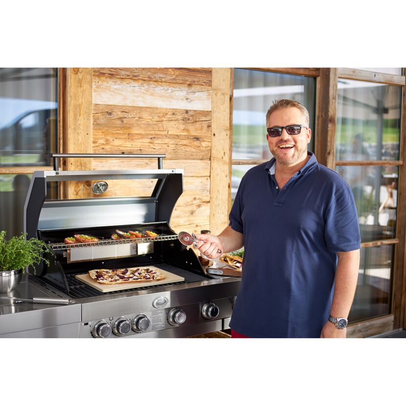 Person mit Pizzaschneider am Gasgrill