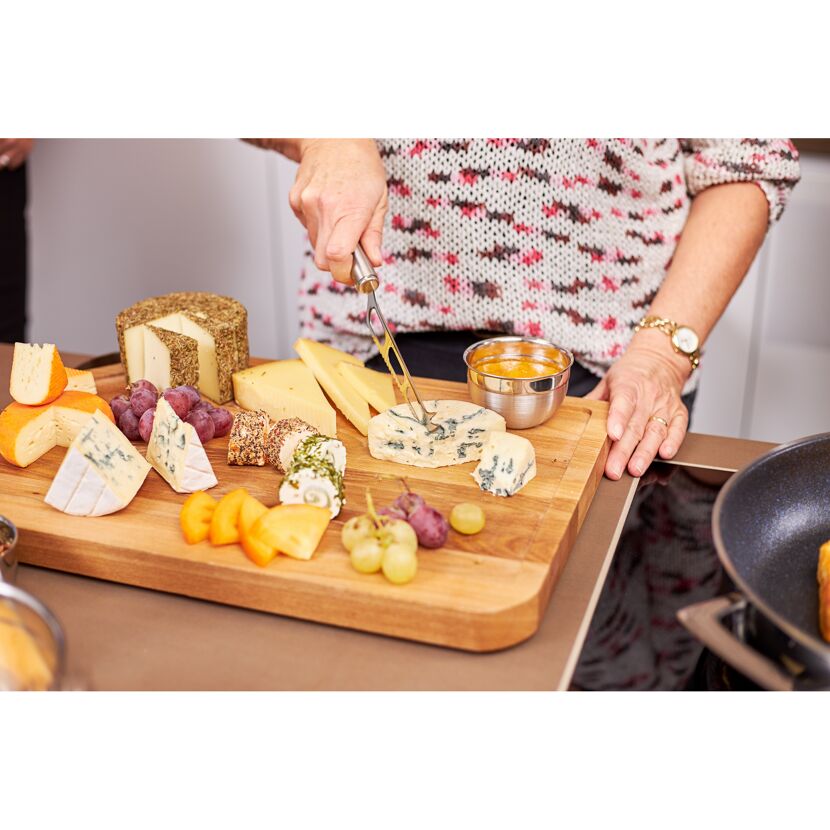 Person schneidet Käse von einer Käseplatte mit einem Käsemesser.