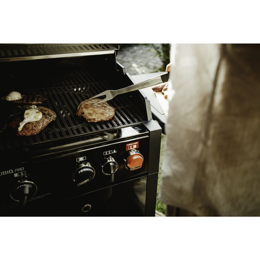 Person grillt Steaks mit Grillgabel auf Gasgrill