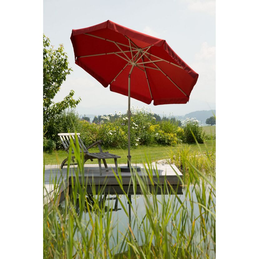 Roter Sonnenschirm und Gartenliege am Wasser