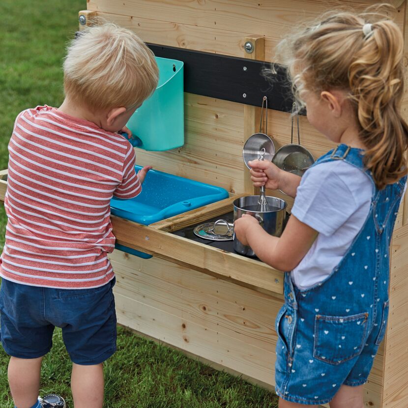 Zwei Kinder spielen mit einer Spielküche im Garten.