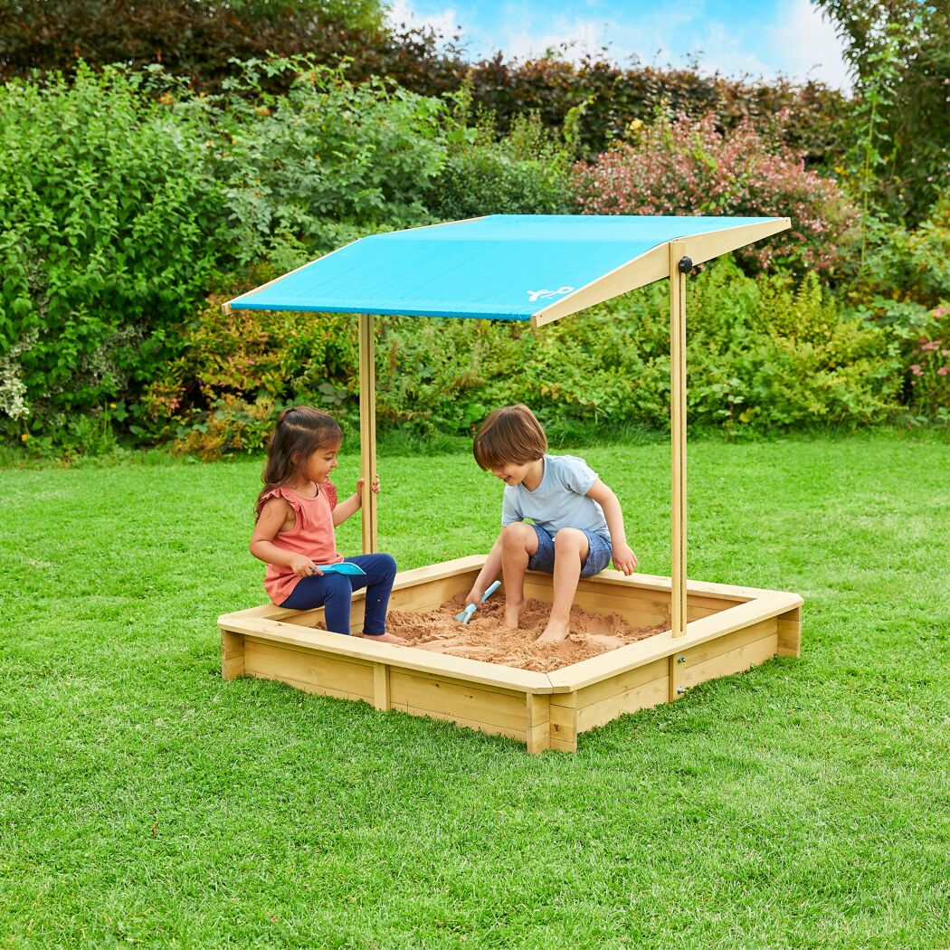 Zwei Kinder spielen in einem Sandkasten mit blauem Sonnendach.