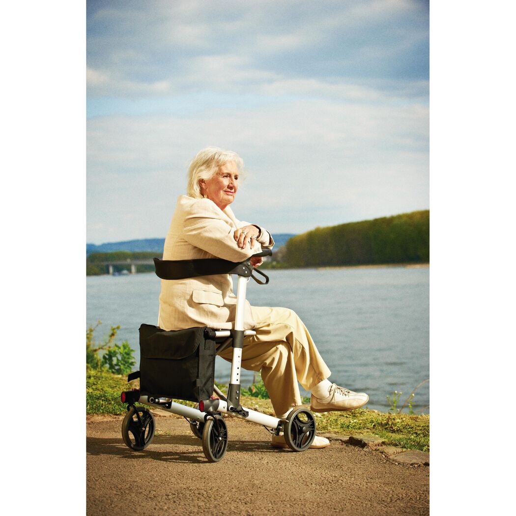 Person sitzt auf Rollator am Flussufer.