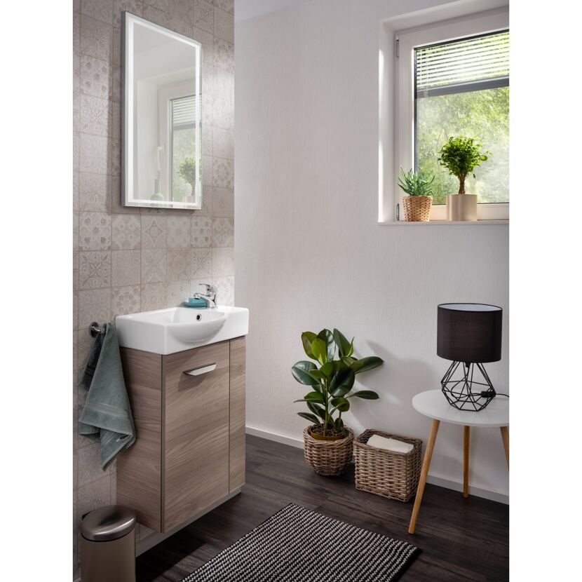 Badezimmer mit beleuchtetem Spiegel, Waschbeckenunterschrank und Deko.