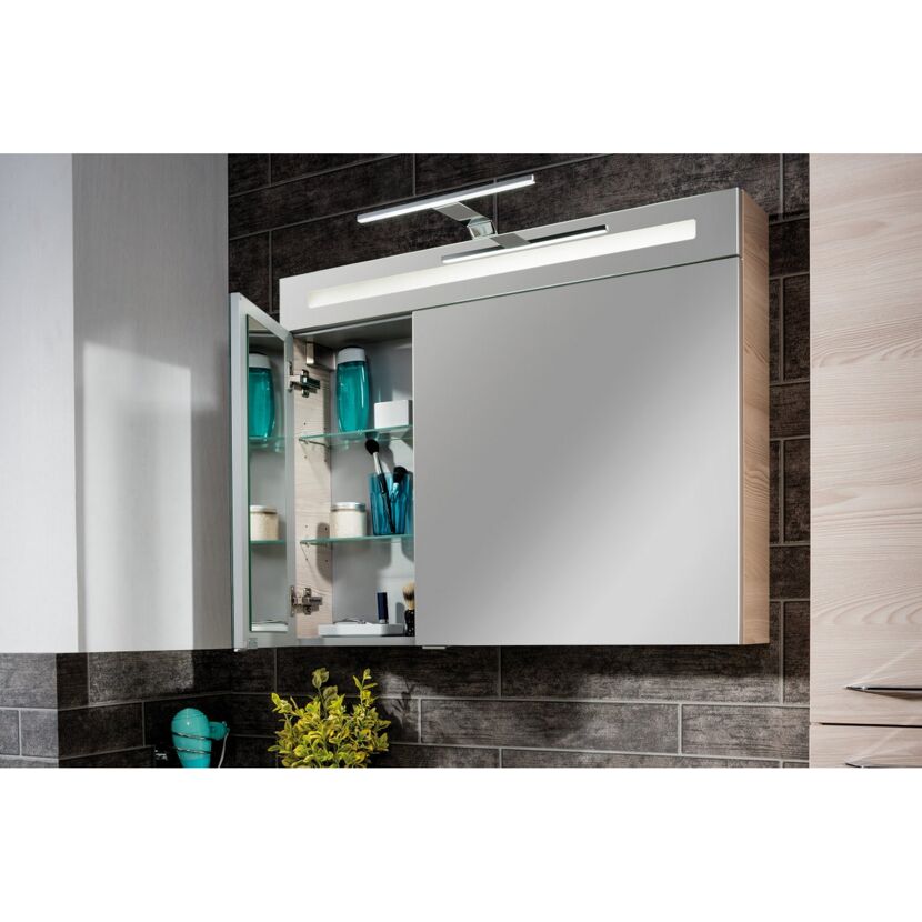 Badezimmerspiegel mit geöffneten Türen und integrierter Beleuchtung. Die Spiegeltüren sind geöffnet und geben den Blick auf die dahinterliegenden Ablagefächer frei, in denen verschiedene Badutensilien wie Flaschen, Tiegel und Pinsel aufbewahrt werden.