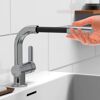 Person hält einen Wasserhahn mit schwarzem, geflochtenen Schlauch.