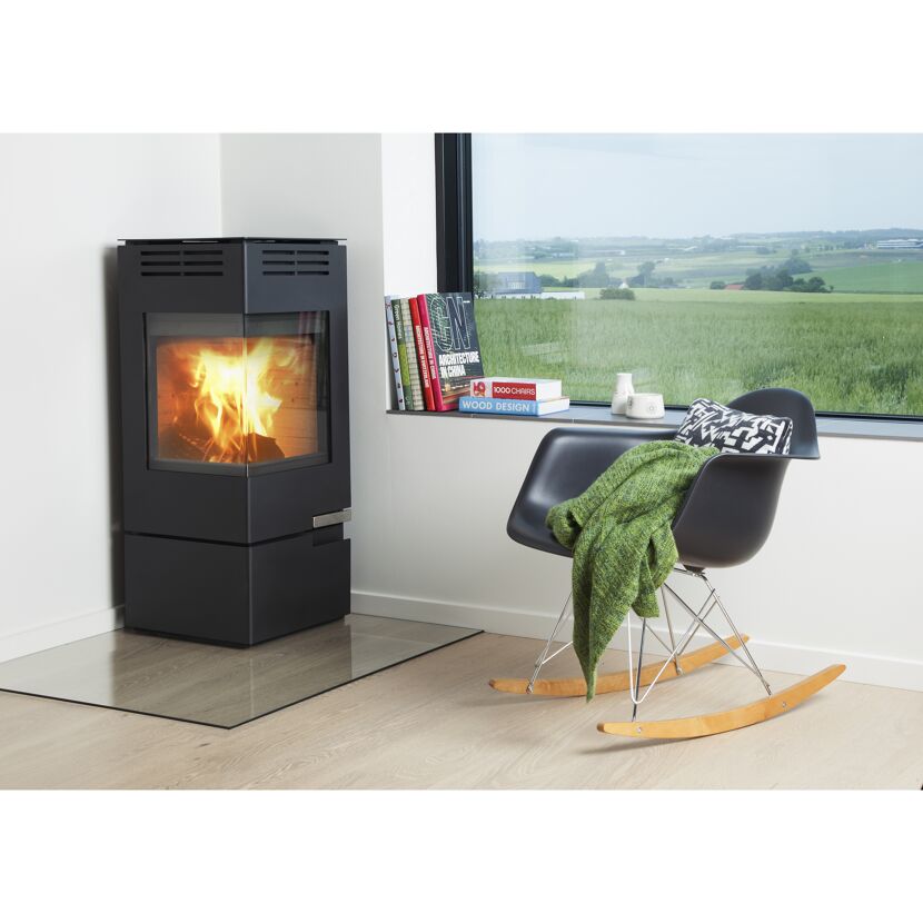 Ein schwarzer Kaminofen Aduro 12 mit Feuer und ein Schaukelstuhl.