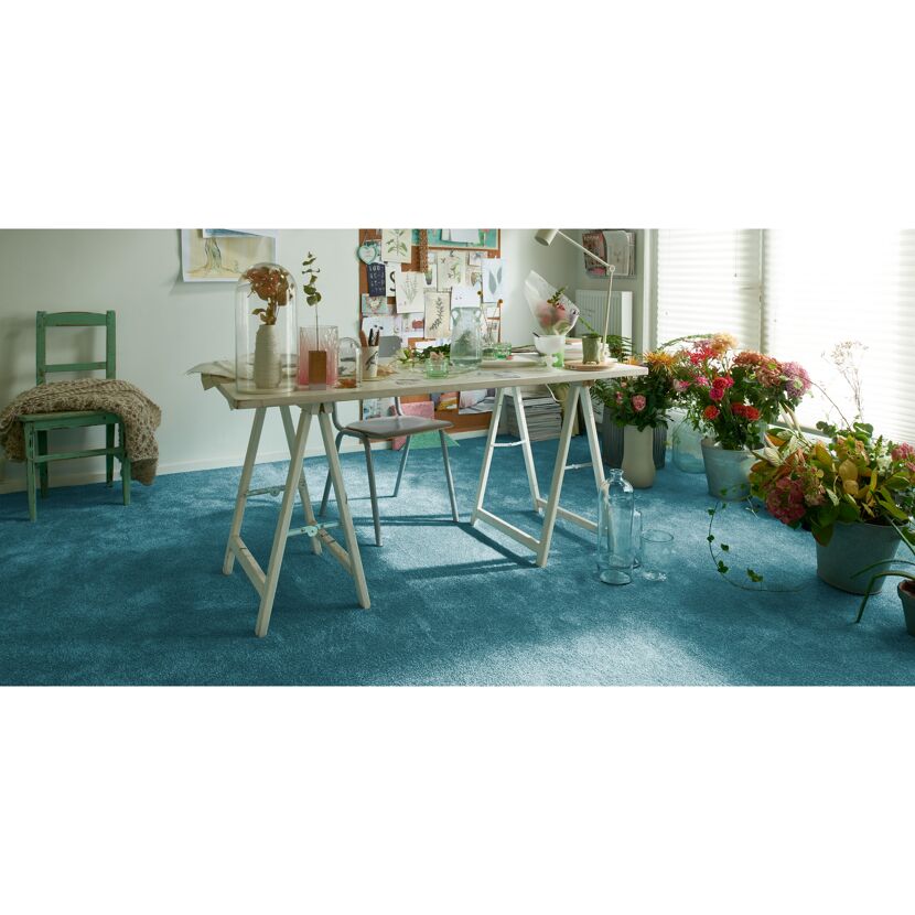 Türkisfarbener Teppichboden in einem Raum mit Blumen und einem Tisch.