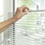 Person verstellt weiße Jalousie am Fenster