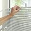 Person verstellt weiße Jalousie am Fenster.