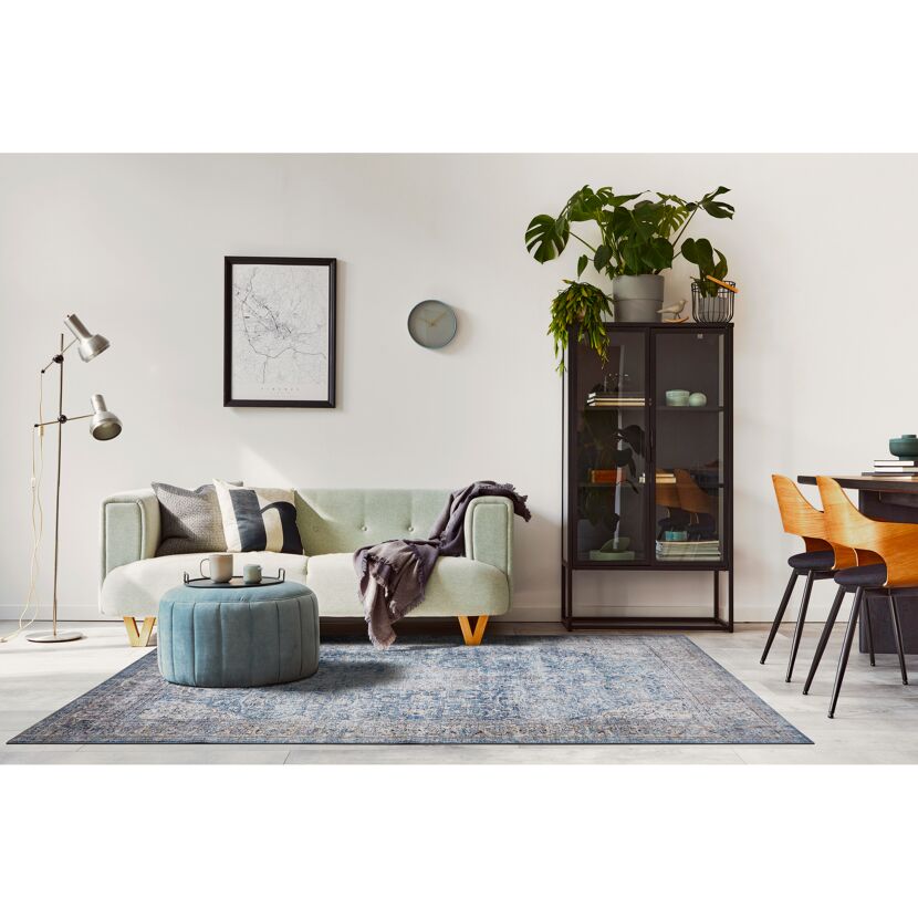 Wohnzimmer mit hellgrünem Sofa, Hocker, Vitrine und gemustertem Teppich