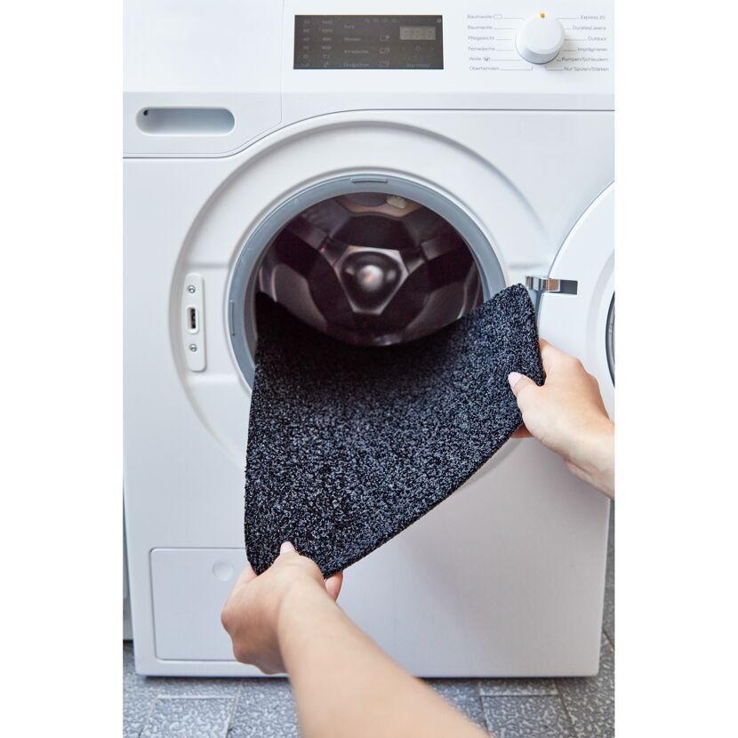 Person legt Fußmatte in Waschmaschine