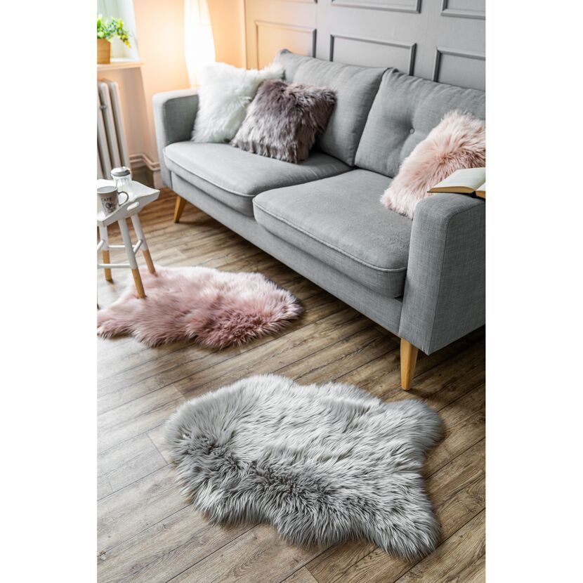 Zwei flauschige Teppiche in Rosa und Grau liegen auf einem Holzfußboden vor einem Sofa.