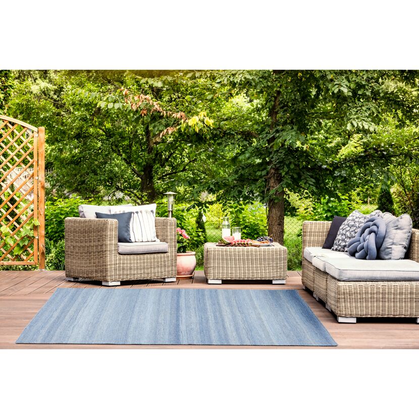 Blauer Teppich auf einer Terrasse mit Gartenmöbeln.