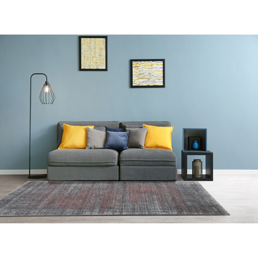 Wohnzimmer mit grauem Sofa, gelben Kissen und grauem Teppich.