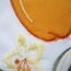 Nahaufnahme von orange-gelben Blumenstickereien auf weißem Stoff.