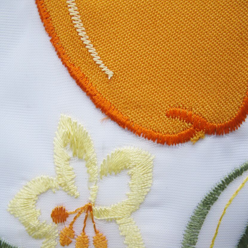 Nahaufnahme von orange-gelben Blumenstickereien auf weißem Stoff.