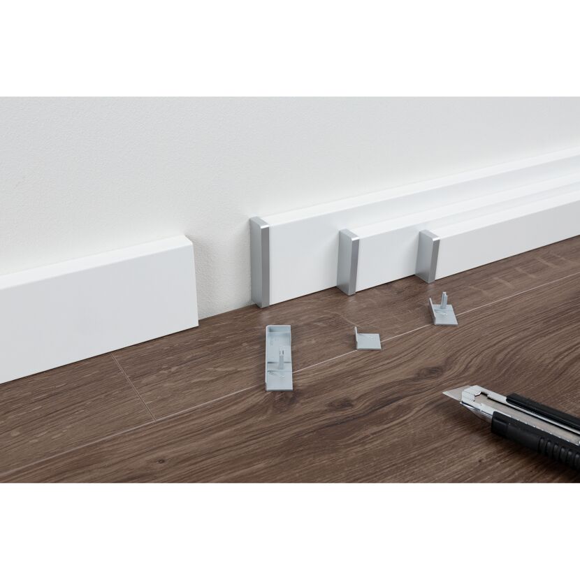 Installation einer weißen Fußleiste mit einem Cuttermesser.