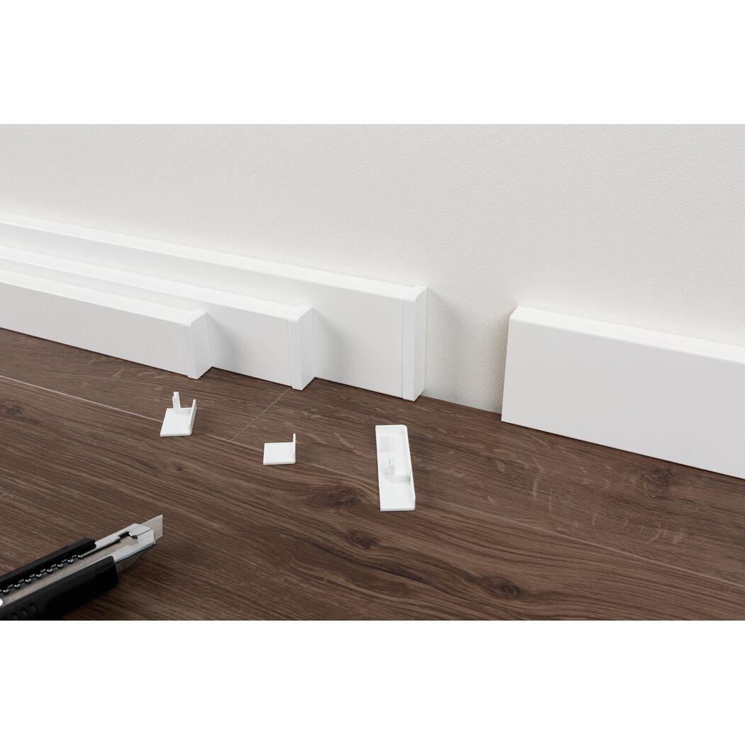 Installation einer weißen Sockelleiste mit einem Cuttermesser.