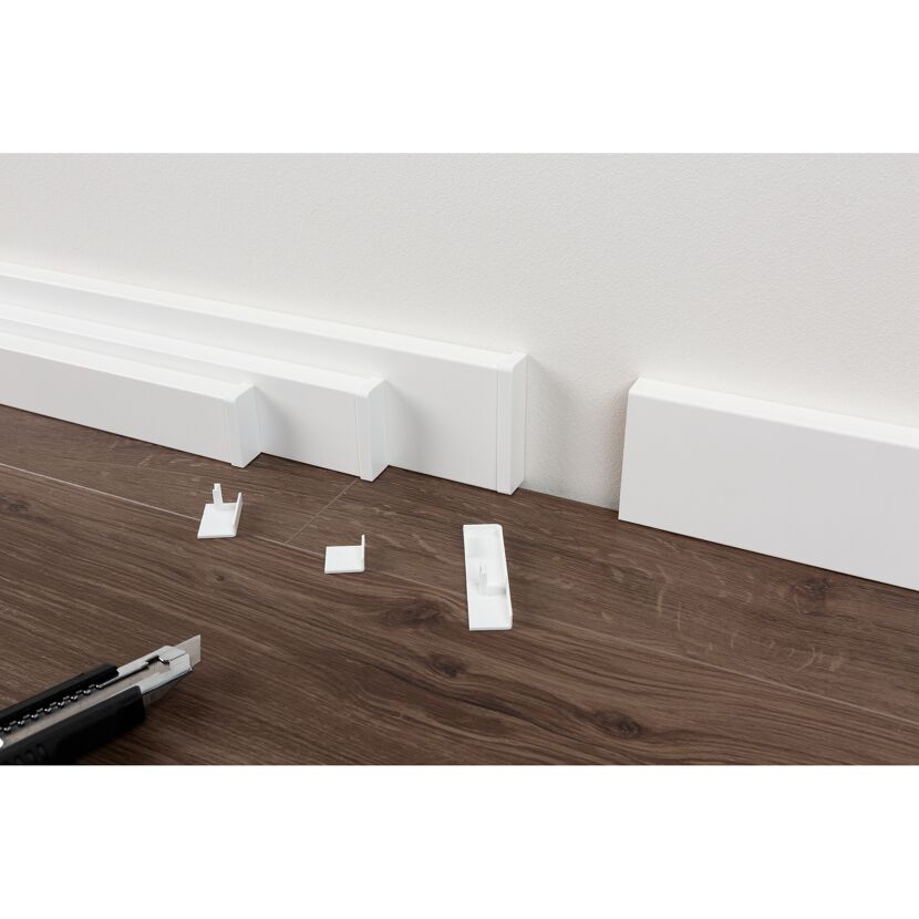 Installation einer weißen Sockelleiste mit einem Cuttermesser.