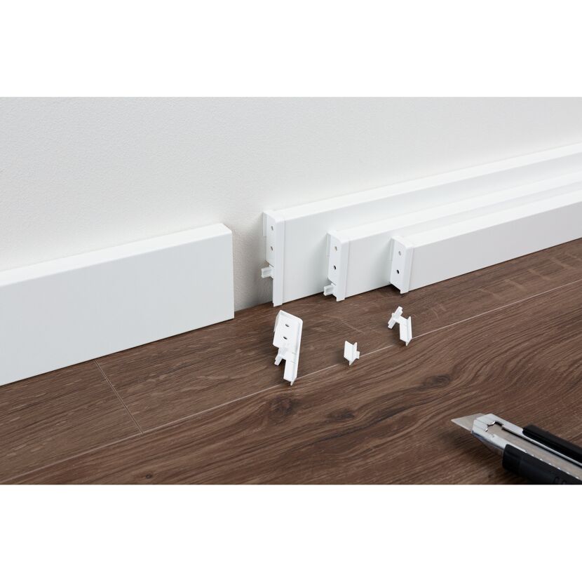 Installation einer weißen Fußleiste mit einem Cuttermesser.