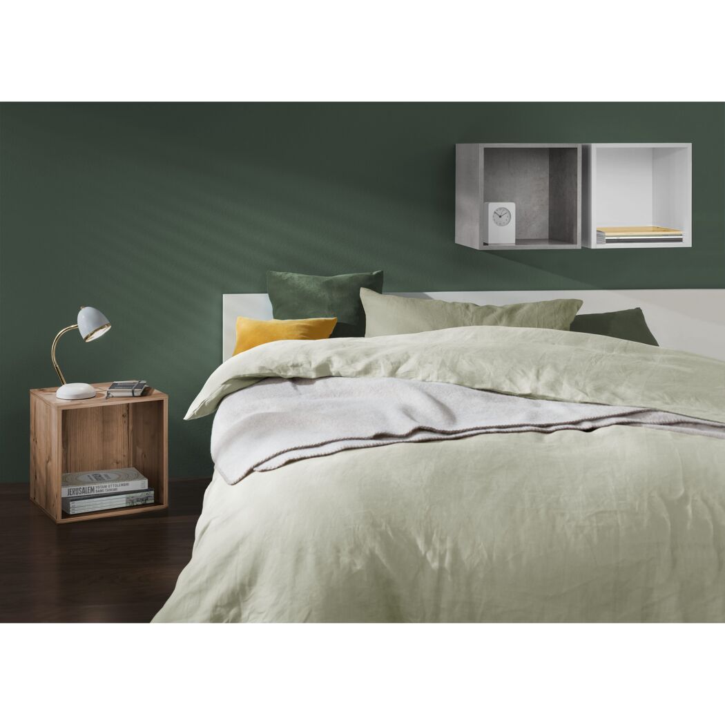 Grünes Schlafzimmer mit hellem Bettzeug und Leselampe