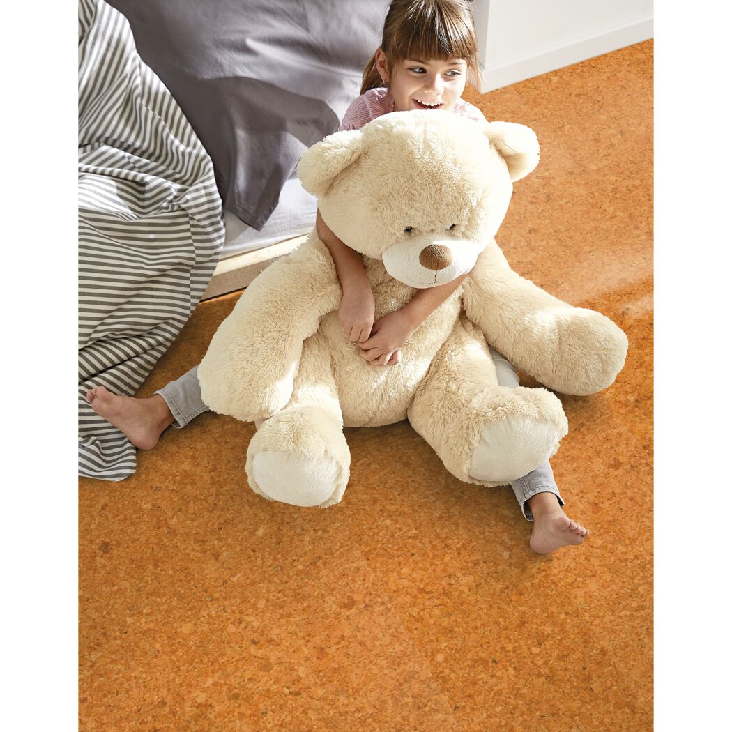 Kind sitzt mit großem Teddy auf Korkparkett