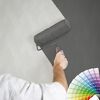 Person streicht mit Farbrolle eine gemusterte Wand grau
