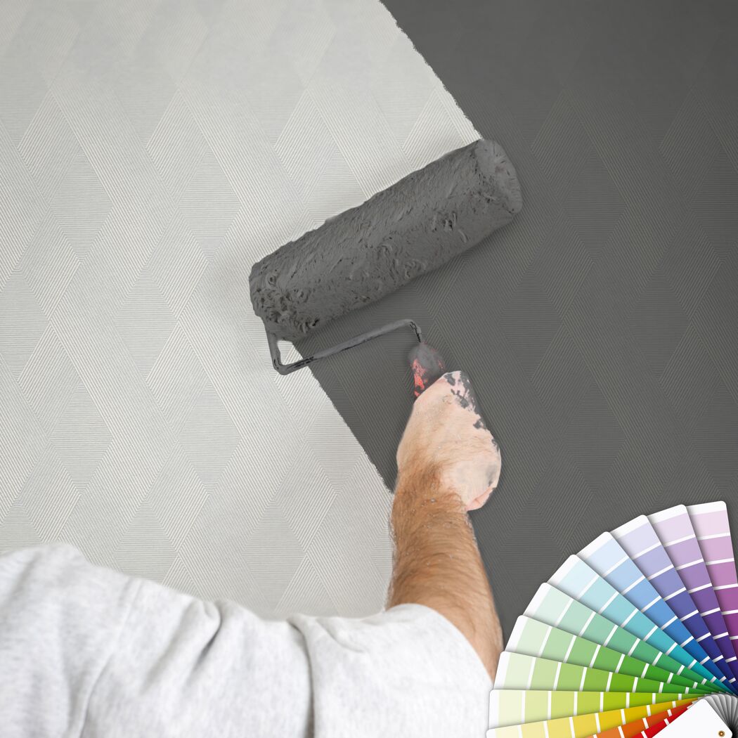 Person streicht mit Farbrolle eine gemusterte Wand grau