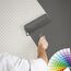 Person streicht mit Farbrolle eine gemusterte Wand grau