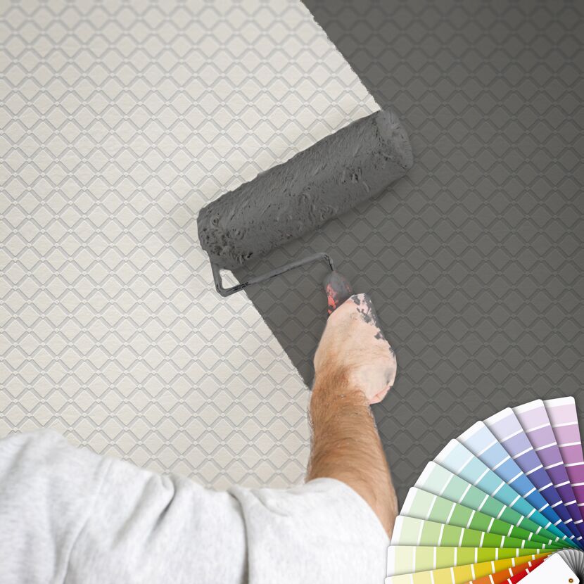 Person streicht mit Farbrolle eine gemusterte Wand grau