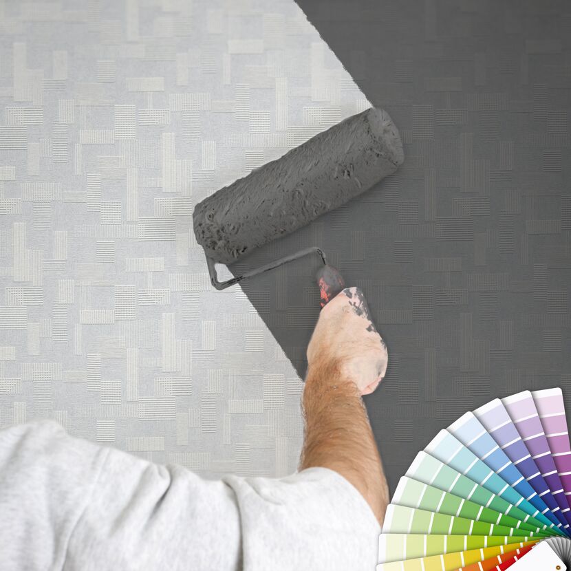 Person streicht Wand mit Farbrolle grau