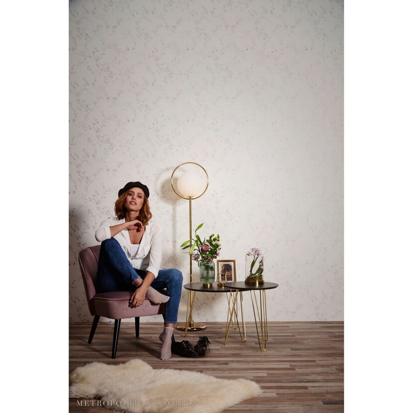 Person sitzt in einem Sessel vor einer Wand mit Blumentapete
