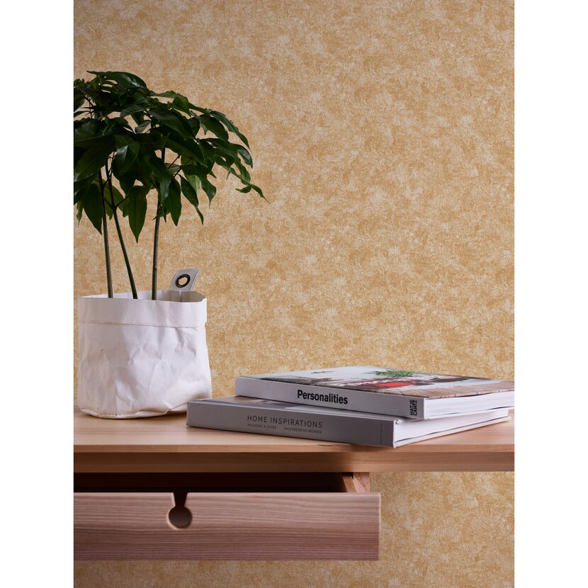 Bücher und Pflanze auf einem Tisch vor einer Wand mit goldener Vliestapete