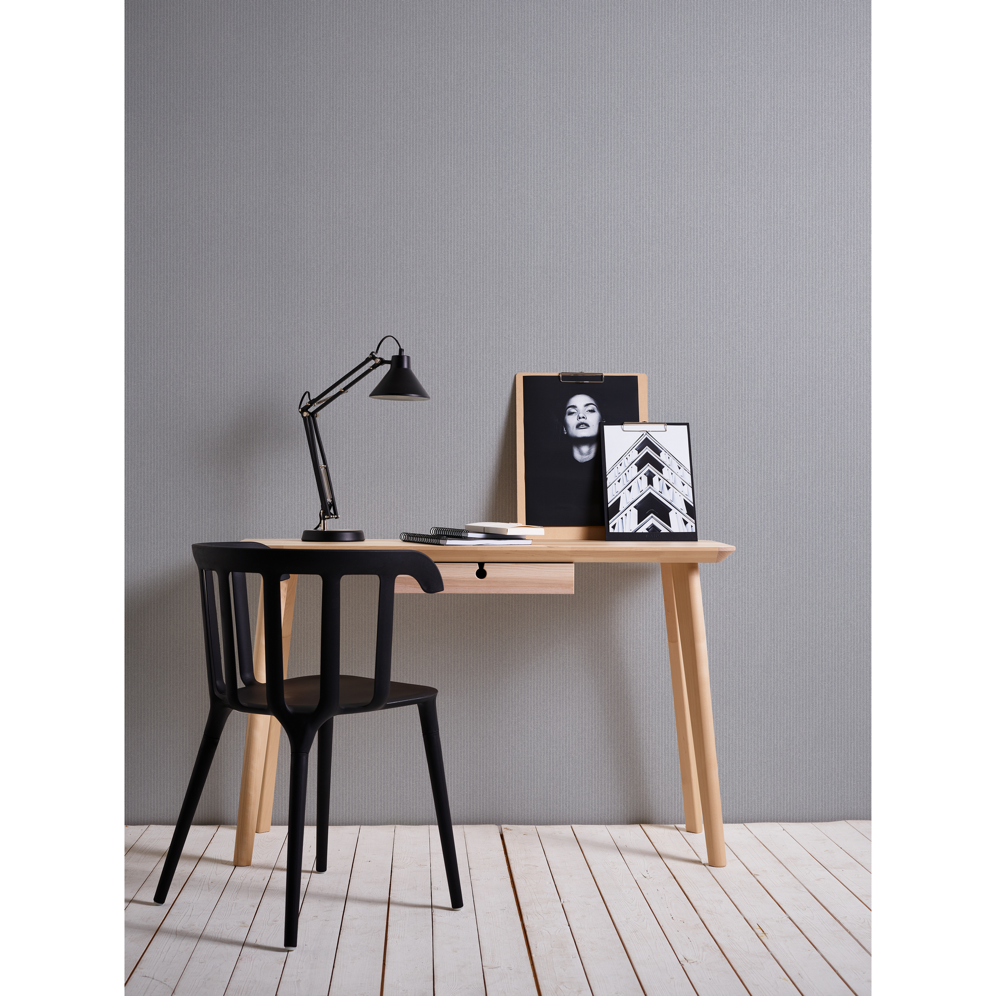 Schreibtisch mit Lampe, Bildern und Stuhl vor grauer Wand