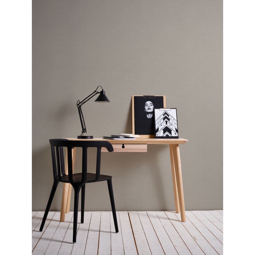 Arbeitsplatz mit Schreibtisch, Lampe und Bildern vor grauer Wand.