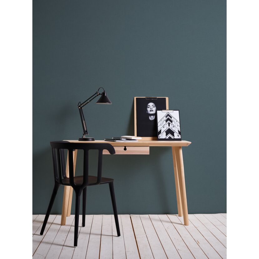 Schreibtisch mit Lampe und Bildern vor petrolfarbener Wand