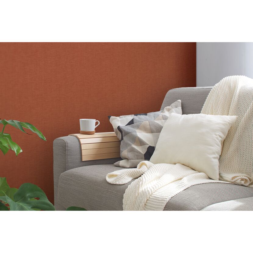 Sofa mit Kissen und Decke vor rotbrauner Wand