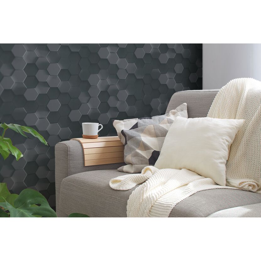 Sofa mit Kissen und Decke vor grauer Wabenwand.