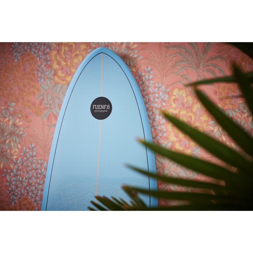 Blaues Surfbrett vor Blumentapete