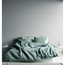 Bett mit blauer Bettwäsche vor grauer Blumentapete