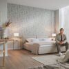 Person sitzt auf Bett in einem Schlafzimmer mit hellgrauer Blumentapete