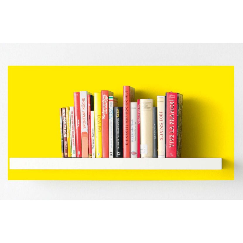Bücherregal mit Kochbüchern vor gelber Wand