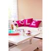 Wohnzimmer mit weißen Sofa und pinken Kissen mit Schriftzug.