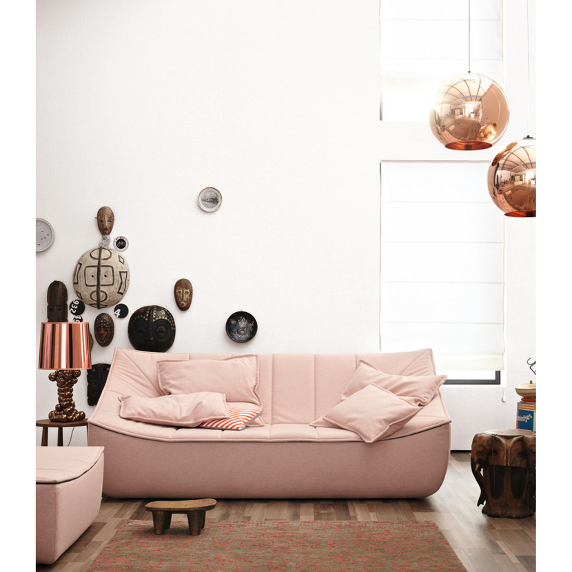 Rosa Sofa mit Deko an der Wand, darunter ein Teppich.